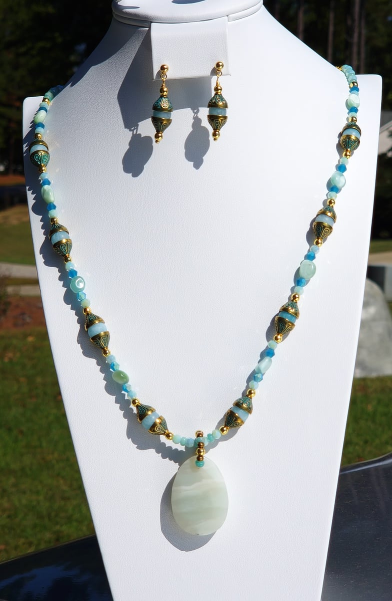 This dynamic necklace and earring set features a Flower Amazonite Pendant, various Amazonite beads, Quartz and 18K Gold Plated Stainless Steel Chain with matching earrings on gold stainless steel ear posts