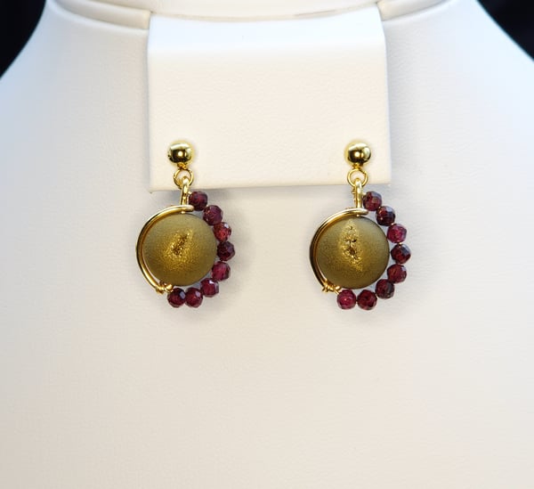 An asymmetrictal design featuring a green/gold Druzy Agate center, garnet accents and stainless steel gold earring post