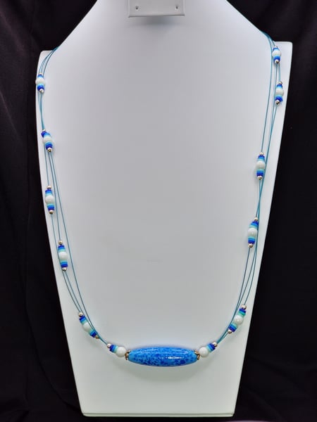 A multi strand necklace featuring a vibrant blue lamp work Glass bead focal