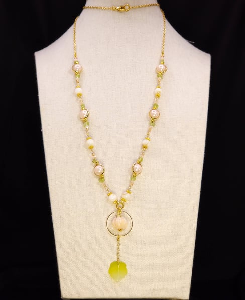 A long gold chain featuring a glass lamp work focal and man made pink pearls